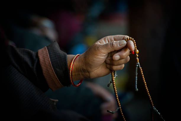 hands of a tibetan buddhist cycles through his prayer beads while chanting.